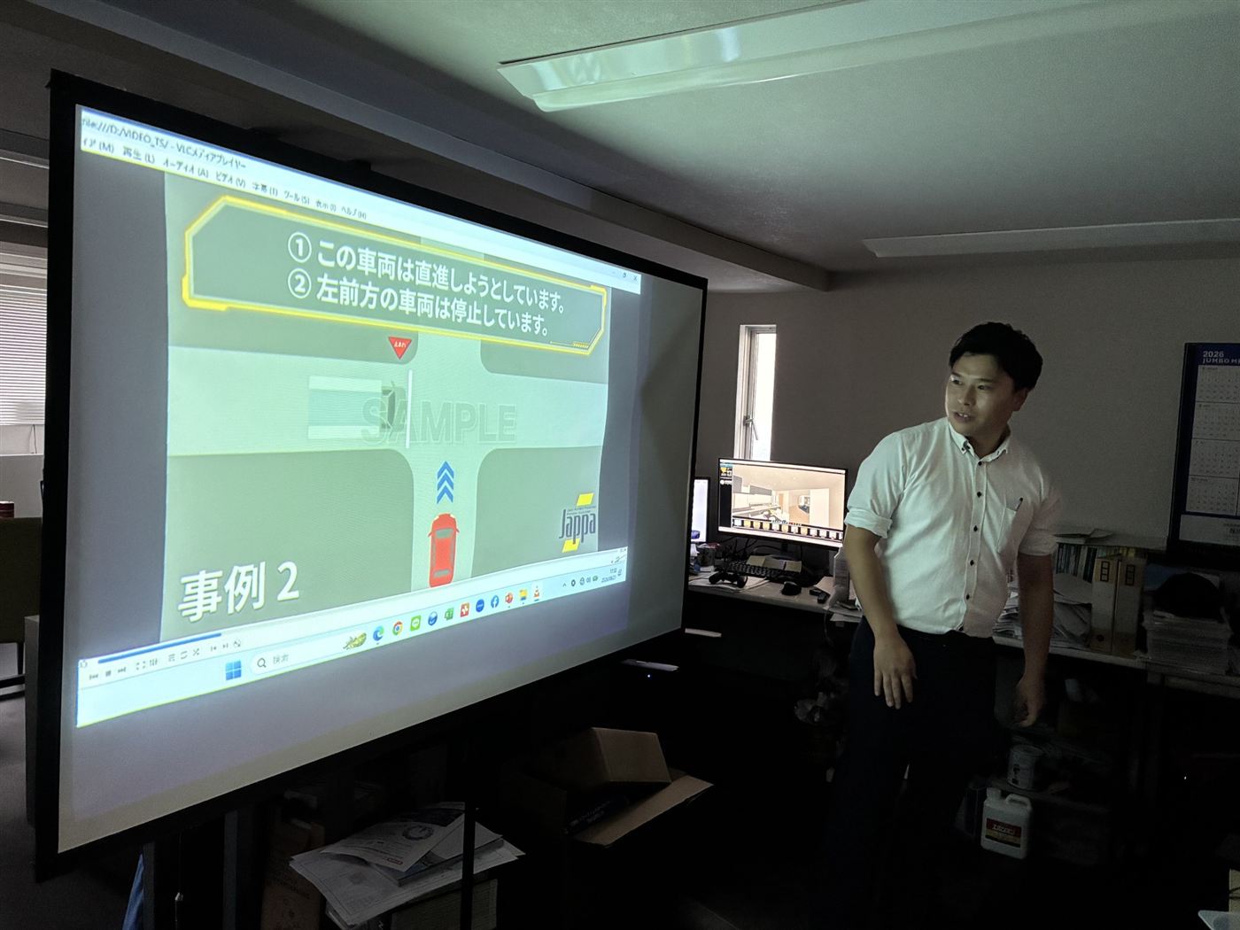 事故事例のアニメーションをスクリーンに映し、解説する当社講師